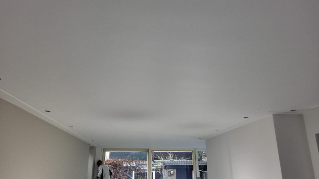 Professionele schilder die strak wit plafond saust in moderne woonkamer