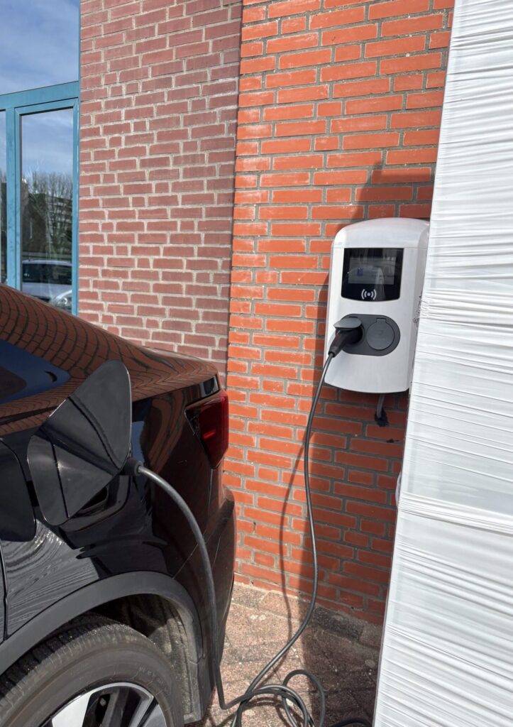 Elektricien die een laadpaal installeert aan de buitenmuur van een woning met zicht op meterkast en bekabeling door offra