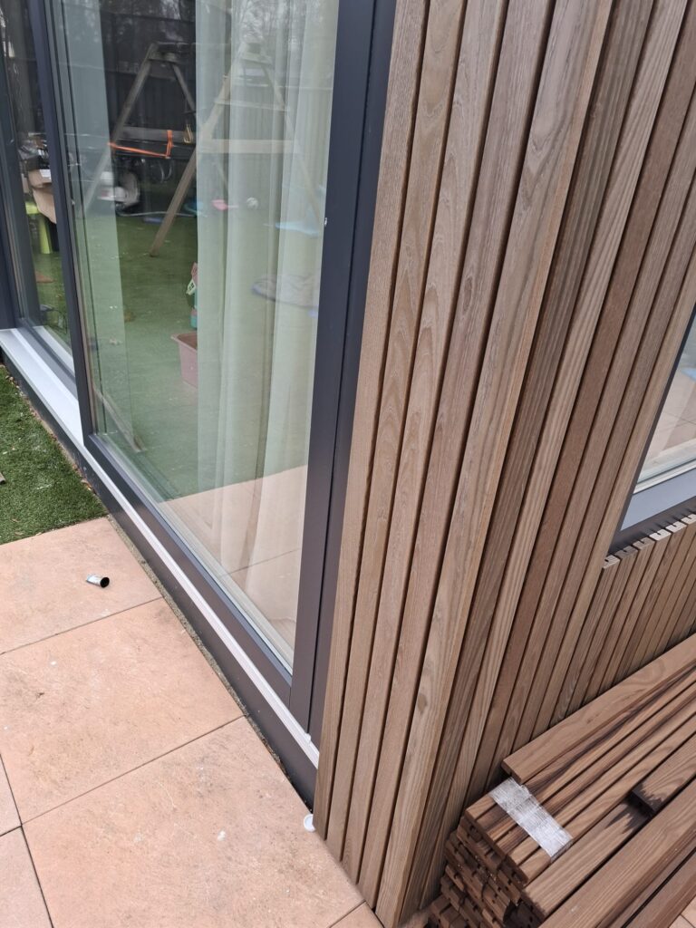 Hoekaanzicht van een moderne aanbouw met houten gevelbekleding en donkere kozijnen.